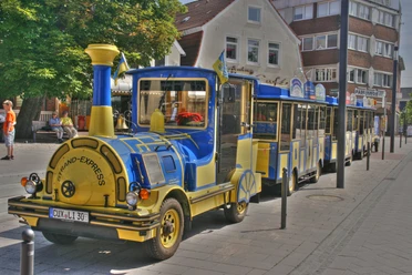 Strand-Express - Cuxliner Ein blauer und gelber Cuxliner Strand-Express parkt auf einer Straße in der Stadt.