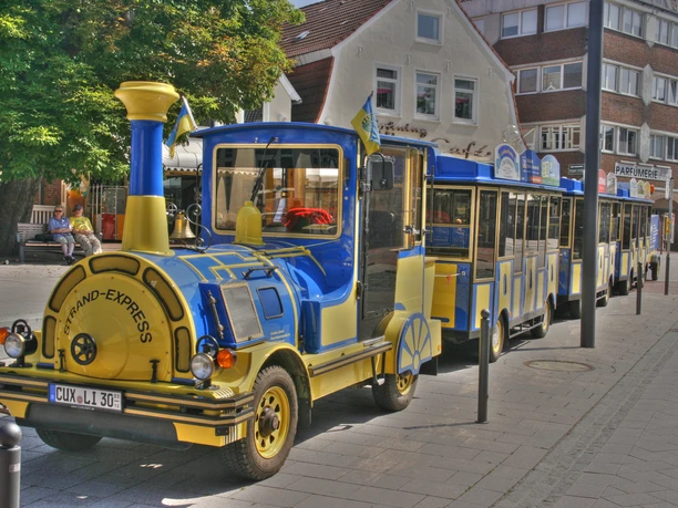 Strand-Express - Cuxliner Ein blauer und gelber Cuxliner Strand-Express parkt auf einer Straße in der Stadt.