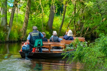 Groep mensen vaart in houten boot door waterkanaal in Sietland onder bomen.