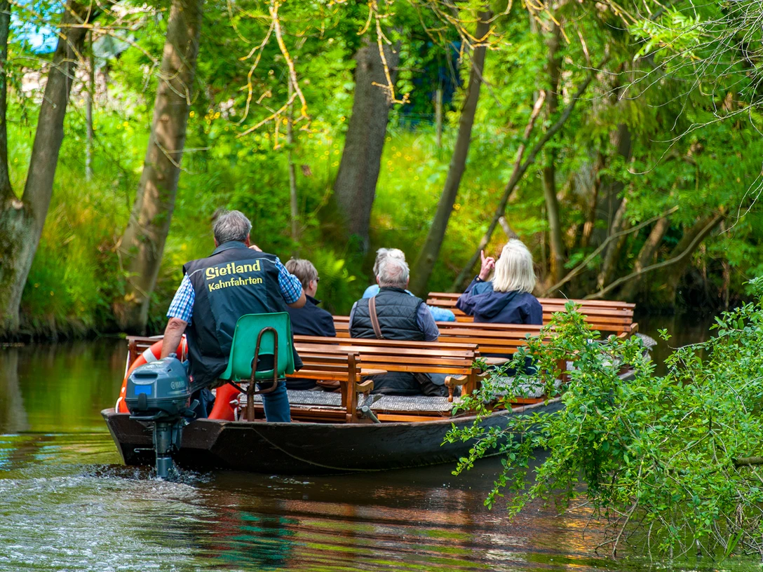 Sietland Kahnfahrt Ihlienworth Personengruppe fährt mit Holzboot durch Wasserkanal im Sietland unter Bäumen.