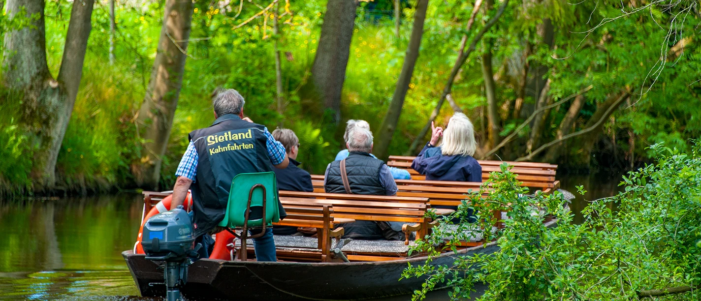 Sietland Kahnfahrt Ihlienworth Personengruppe fährt mit Holzboot durch Wasserkanal im Sietland unter Bäumen.