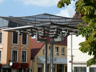 Achimer Glockenspiel Ein modernes Glockenspiel mit mehreren Glocken vor historischen Stadthäusern in Achim bei sonnigem Wetter.