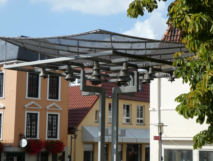 Achimer Glockenspiel Ein modernes Glockenspiel mit mehreren Glocken vor historischen Stadthäusern in Achim bei sonnigem Wetter.
