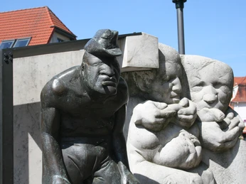 Bronzeskulptur eines Zigarrenmachers und Kindern in rustikaler Straßenszene mit roten Ziegeldächern.