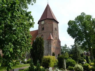 Backsteinkirche mit markantem Turm und rotem Dach, umgeben von gepflegtem Grün und Baumbestand.