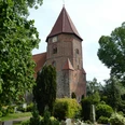 Backsteinkirche mit markantem Turm und rotem Dach, umgeben von gepflegtem Grün und Baumbestand.