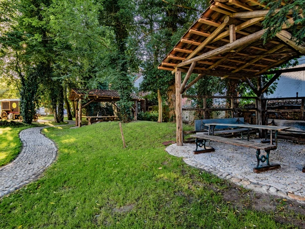 Alte Drostei Gepflasterter Weg führt durch schattigen Garten mit Holzpavillons und rustikalen Sitzbänken.