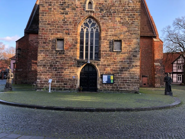 Backsteingebäude mit spitzem Dach und einer Statue auf jeder Seite, bei sonnigem Wetter fotografiert.