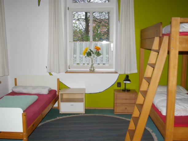 Dreibettzimmer Dreibettzimmer mit Einzelbett, Etagenbett, grün-weißer Wand und Fenster.