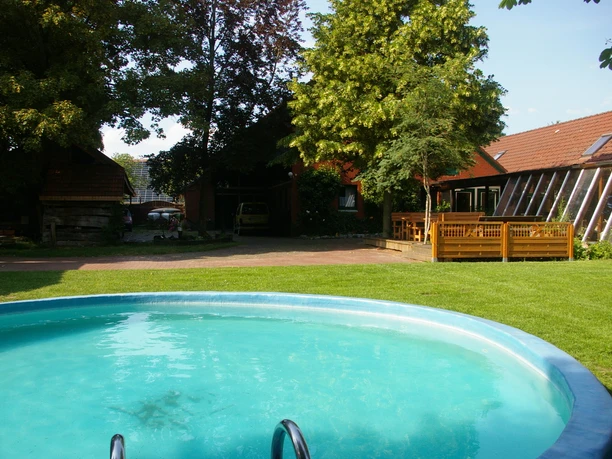Innenhof mit Pool Runder Pool im grünen Innenhof mit Bäumen, Rasen und Backsteingebäuden.