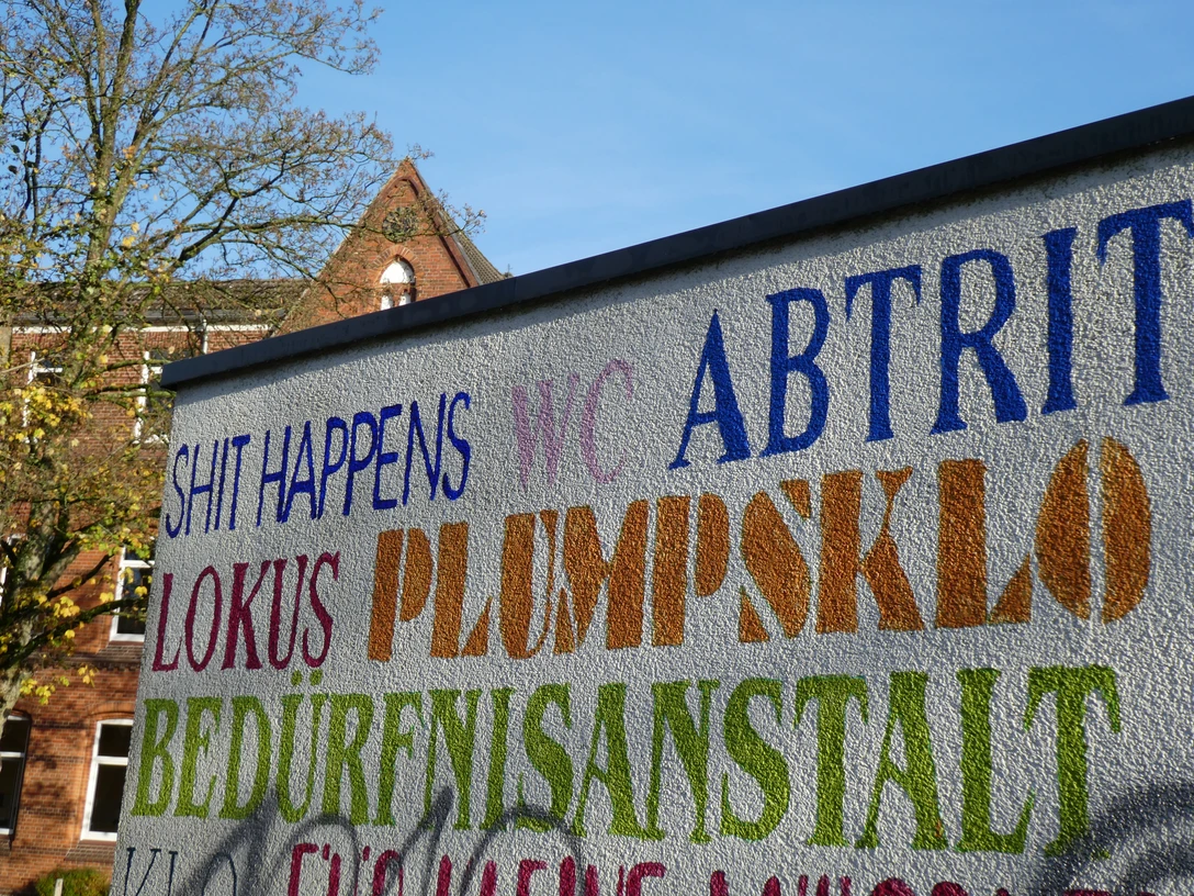 Bunte Schriftzüge auf einer Wand markieren ein öffentliches WC in der Nähe des Rathauses von Achim.