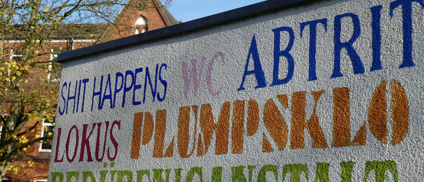 Öffentliches WC Parkplatz Rathaus Achim Bunte Schriftzüge auf einer Wand markieren ein öffentliches WC in der Nähe des Rathauses von Achim.