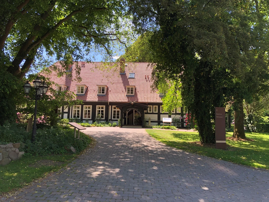 Ein traditionelles Fachwerkhaus mit rotem Ziegeldach, eingebettet in üppigem, grünen Baumbestand.