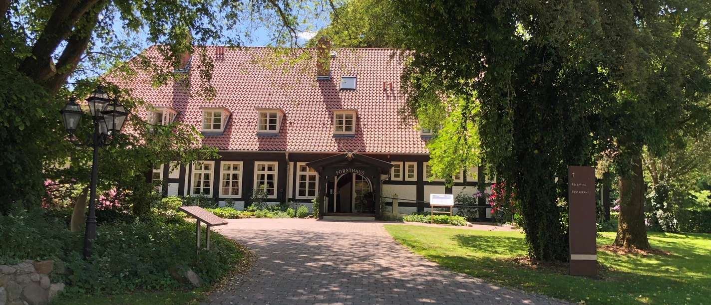 A traditional half-timbered house with a red tiled roof, nestled among lush, green trees.