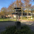 Skulptur "Juvenil" Stählerne Skulptur auf einem Sockel in herbstlicher Parkanlage, umgeben von Bäumen und Gebäuden.