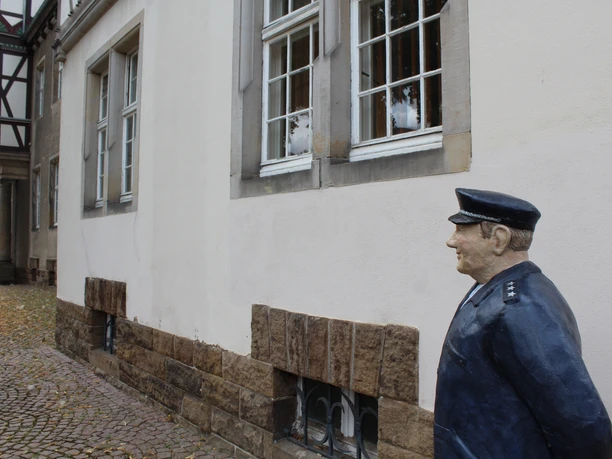 Wachmeister Schulze Eine Skulptur eines Polizeiwächters steht vor einem alten Fachwerkgebäude in Petershagen.