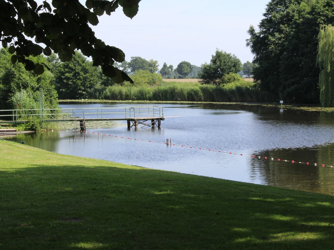 Badestelle am Blender See mit Steg, umgeben von grüner Wiese und Bäumen, lädt zum Entspannen ein.