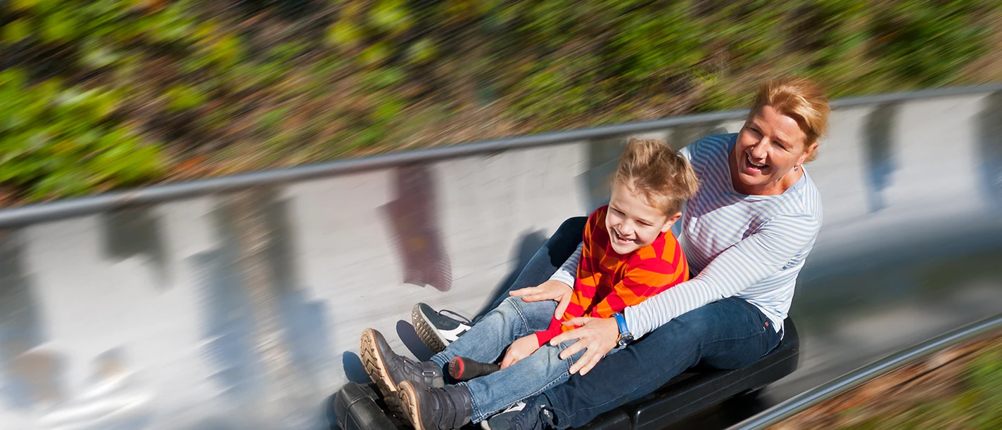 Spielpark Wingst Rodelbahn Frau und Kind sausen lachend auf der Sommerrodelbahn im Spielpark Wingst durch die Kurve.