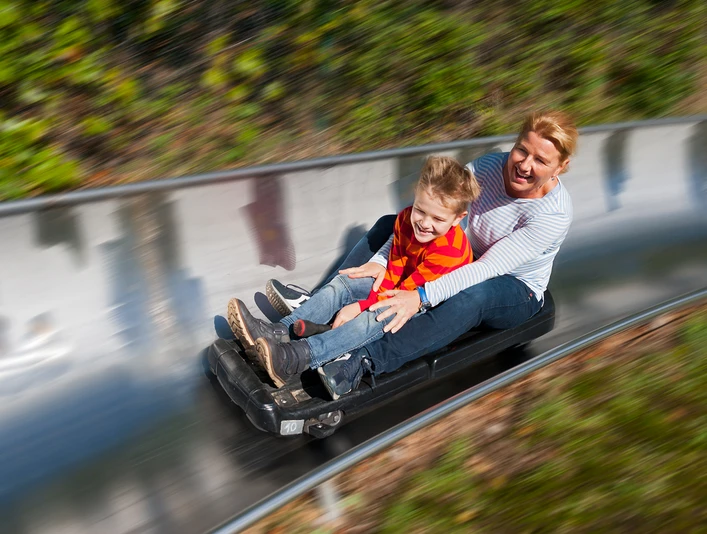 Spielpark Wingst Rodelbahn Frau und Kind sausen lachend auf der Sommerrodelbahn im Spielpark Wingst durch die Kurve.
