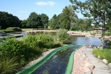 Naturerlebnisbad Rodewald mit grünem Wasserrutschenbereich, umgeben von Bäumen und Wasserflächen.