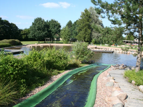 Naturerlebnisbad Rodewald mit grünem Wasserrutschenbereich, umgeben von Bäumen und Wasserflächen.