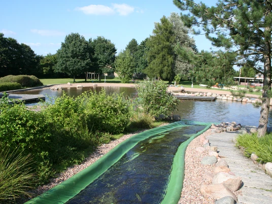 Naturerlebnisbad Rodewald Naturerlebnisbad Rodewald mit grünem Wasserrutschenbereich, umgeben von Bäumen und Wasserflächen.