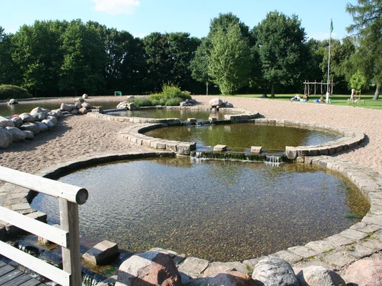Naturerlebnisbad Rodewald Naturbad mit organisch gestalteten Becken, umgeben von Sand und Grün, lädt zur Erholung im Freien ein.
