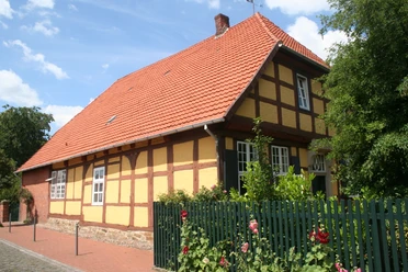 Münchhausenhof in Stolzenau Fachwerkhaus mit roten Ziegeln, umgeben von Rosensträuchern und grünem Zaun unter blauem Himmel.