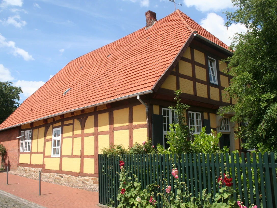 Münchhausenhof in Stolzenau Fachwerkhaus mit roten Ziegeln, umgeben von Rosensträuchern und grünem Zaun unter blauem Himmel.
