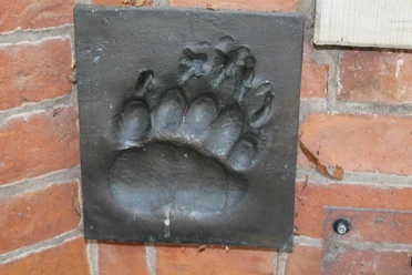 Bronze Relief Bärentatze Ein in eine Ziegelwand eingelassenes Bronzereflief zeigt den detaillierten Abdruck einer Bärentatze.