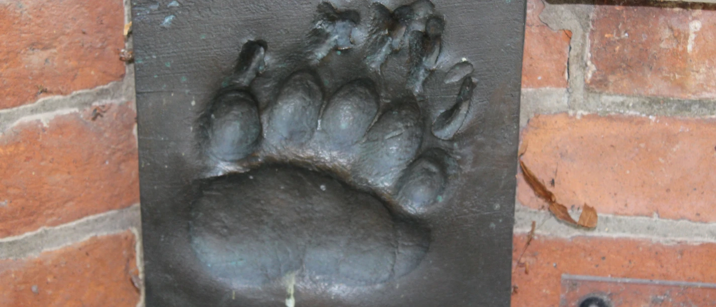 Bronze Relief Bärentatze A bronze relief set into a brick wall shows the detailed imprint of a bear's paw.