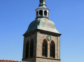 Aegidiuskirchen Wiedenbrück Ein Kirchturm mit Kupferdach und Glocken aus der Perspektive hinter roten Ziegeldächern.