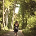 Wandern in Ostercappeln Eine Person mit langen Haaren geht auf einem Waldweg im Sonnenlicht spazieren.