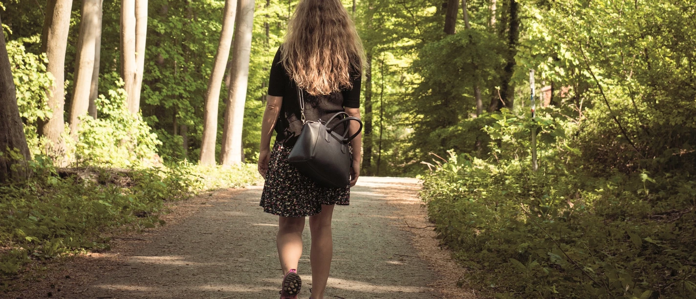 Wandern in Ostercappeln Eine Person mit langen Haaren geht auf einem Waldweg im Sonnenlicht spazieren.