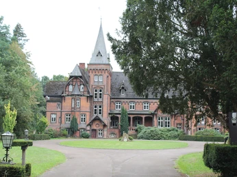 Historisches Schloss Eickhof mit markantem Turm, umrahmt von prächtigen Bäumen und gepflegtem Garten.