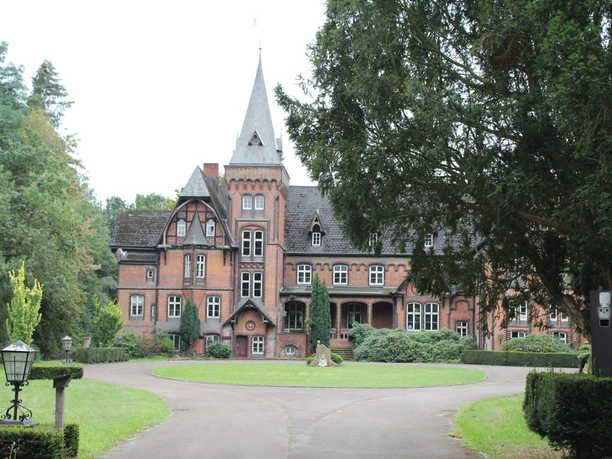 Historisches Schloss Eickhof mit markantem Turm, umrahmt von prächtigen Bäumen und gepflegtem Garten.