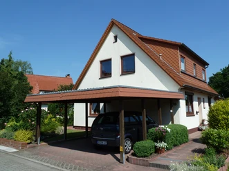 Vrijstaand huis met carport en verzorgde tuin, onder een blauwe hemel in een rustige buurt.