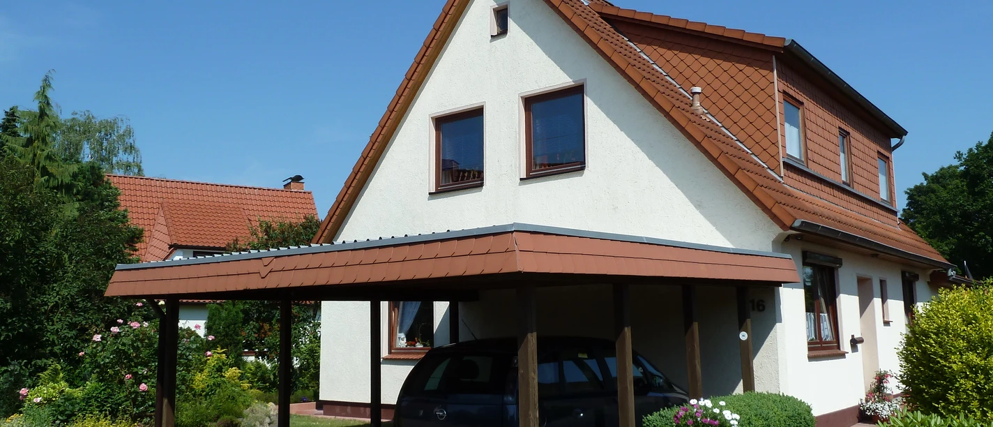 Detached house with carport and well-kept garden, under a blue sky in a quiet environment.