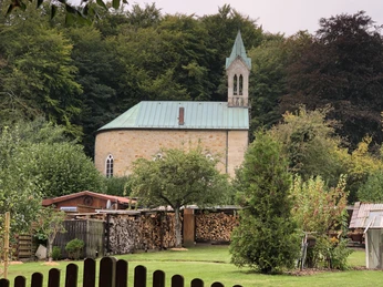 Friederikenkapelle Eine Kapelle steht malerisch inmitten von Bäumen, mit einem kleinen Turm und grünem Dach.
