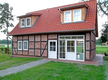 Ferienhaus Wikner Fachwerkhaus mit rotem Ziegeldach und weißen Fenstern, umgeben von grünem Landschaftsambiente.Half-timbered house with red tiled roof and white windows, surrounded by green countryside.Bindingsværkshus med rødt tegltag og hvide vinduer, omgivet af grønt landskab.Vakwerkhuis met rood pannendak en witte ramen, omgeven door groen platteland.