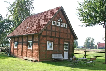 Ferienhof Wikner Fachwerkhaus auf einem grünen Hof mit Gartenmöbeln, umgeben von Bäumen und ländlicher Landschaft.