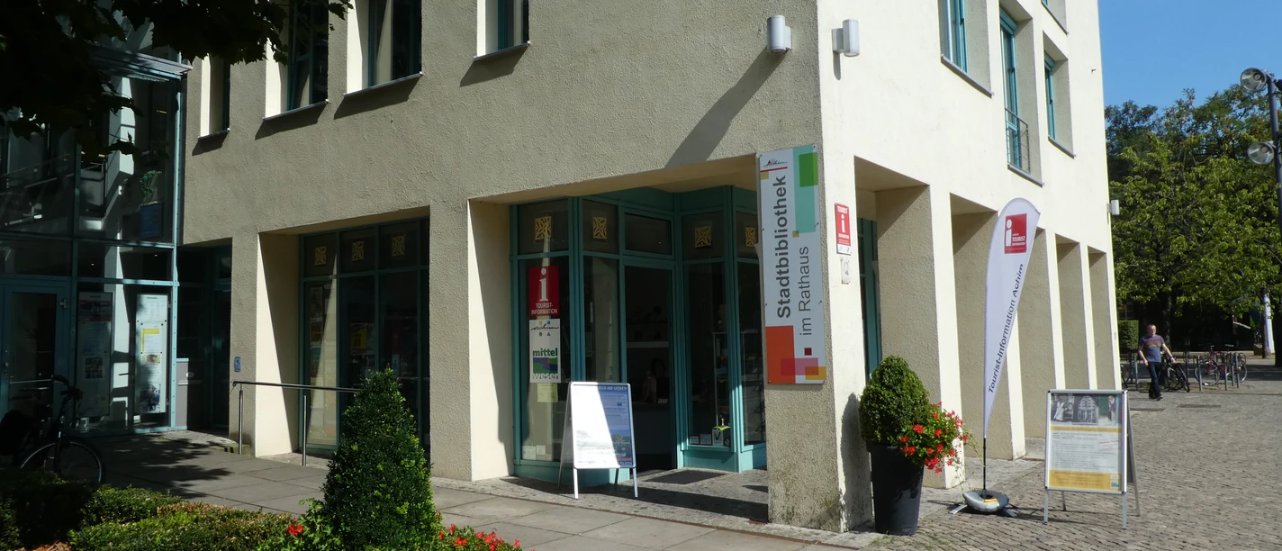 Tourist-Information Achim Eingang der Tourist-Information Achim, einladend dekoriert mit Blumenkübeln und Infotafeln.