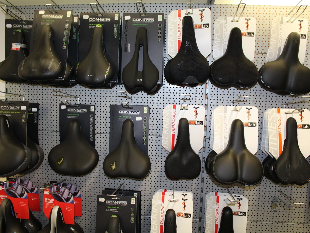 Fahrradzubehör Verschiedene Fahrradsättel in einem Geschäft, ordentlich in Regalen angeordnet, an einer Wand ausgestellt.