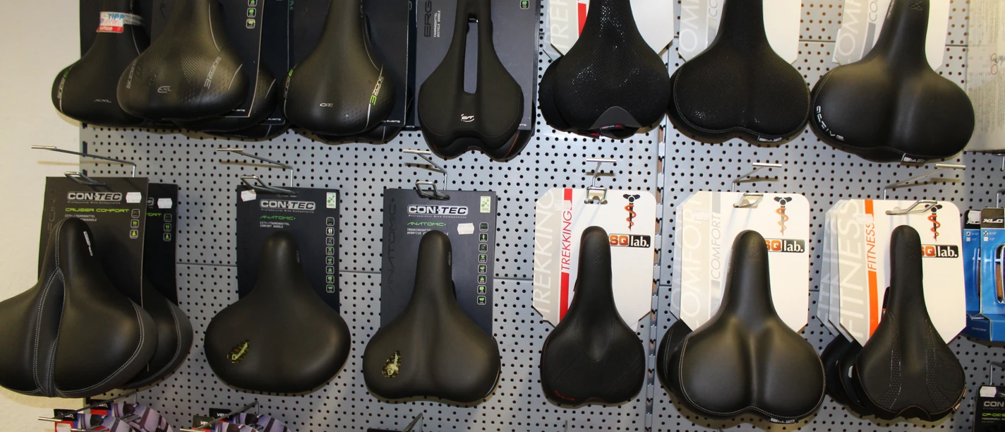 Fahrradzubehör Verschiedene Fahrradsättel in einem Geschäft, ordentlich in Regalen angeordnet, an einer Wand ausgestellt.