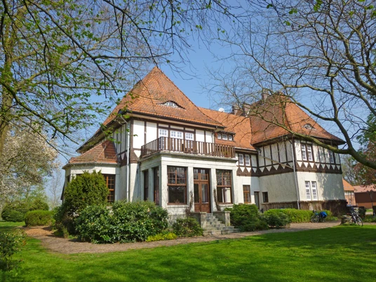 Gut Lohof Ein historisches Gutshaus mit Fachwerkelementen und roten Ziegeldächern in einer grünen Parkanlage.