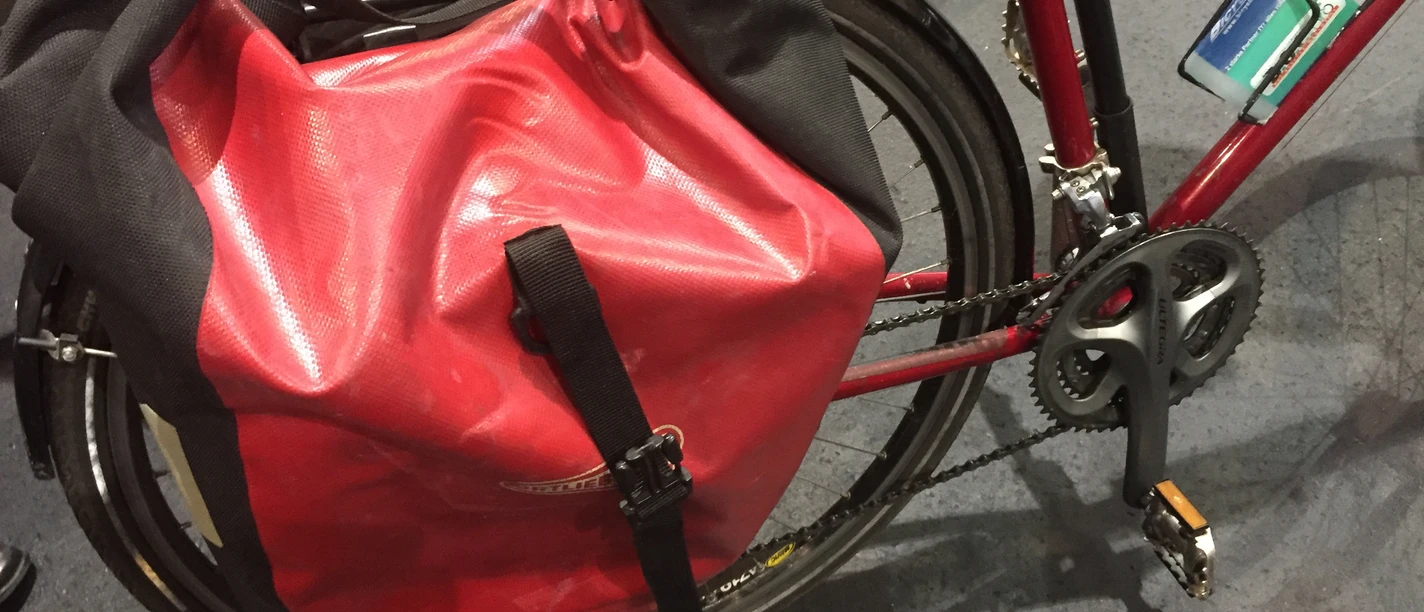 A red bicycle bag made of waterproof material attached to a bicycle frame, protected from the rain.