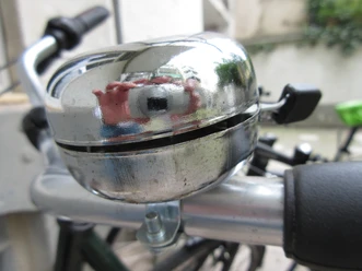 Silberne Fahrradklingel auf einem Lenker, leicht abgenutzt mit einer reflektierenden Oberfläche.