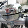 Silberne Fahrradklingel auf einem Lenker, leicht abgenutzt mit einer reflektierenden Oberfläche.