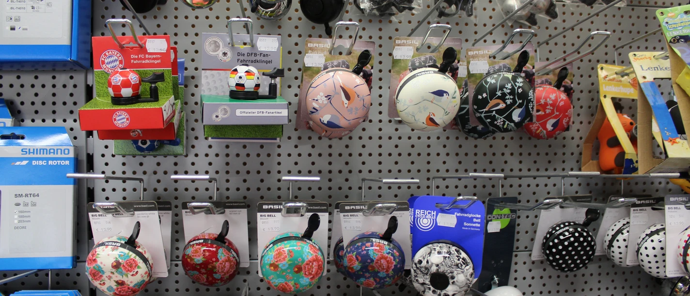 Fahrradzubehör Eine große Auswahl an Fahrradklingeln und Zubehör hängt ordentlich an einer perforierten Wand.