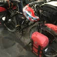 Ein schwarzes Touringrad mit roter Fahrradtasche und Helm steht gepackt auf einem Boden aus grauem Asphalt.